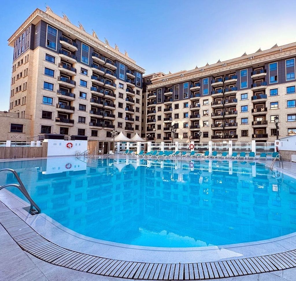 Une piscine avec des chaises longues et, au fond, un bâtiment doté de nombreux balcons.