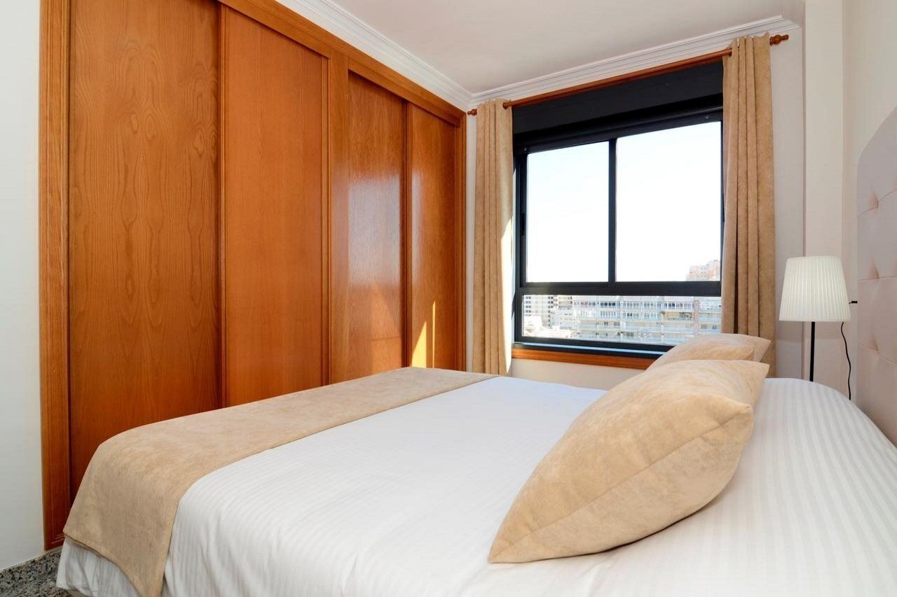 Ein Hotelzimmer mit einem großen Bett, Holzwänden, einem Fenster mit Blick auf Gebäude und einer Nachttischlampe.