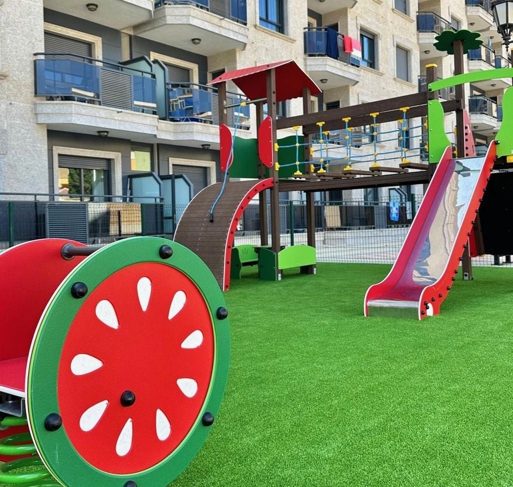 Une aire de jeux avec un toboggan et des structures d’escalade, entourée d’une pelouse artificielle verte.