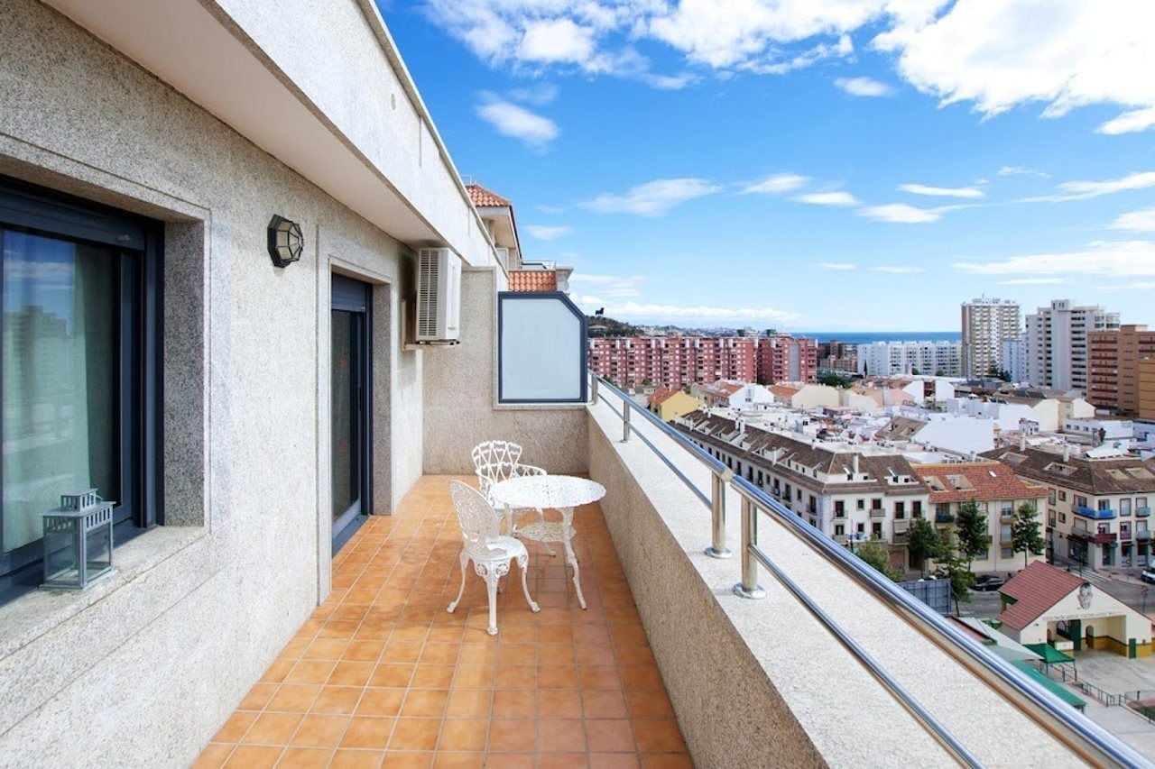 Een balkon met een tafel en stoelen, met uitzicht op een stadsbeeld met gebouwen en een heldere lucht.