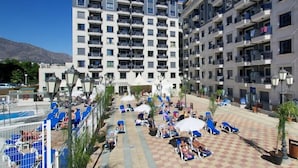 A hotel with multiple floors, outdoor pool area with sun loungers, and a clear view of mountains in the background. - Apartamentos Nuriasol (Fuengirola)