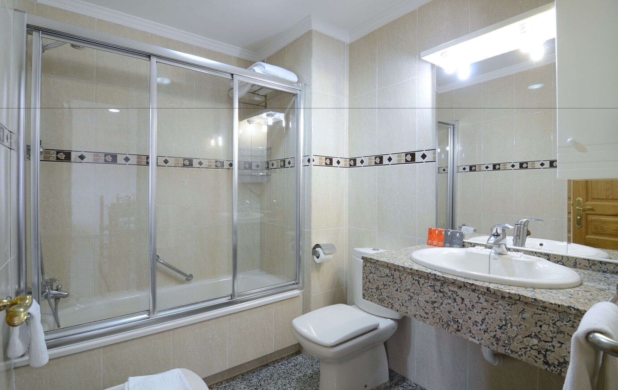 Une salle de bain avec une douche à parois de verre, un lavabo avec un plan de toilette en marbre et des toilettes.