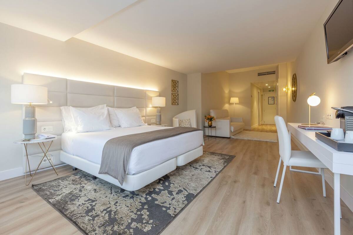 A modern hotel room with a large bed, bedside tables, a desk, and a chair.