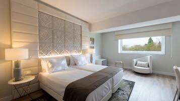 Habitación de hotel moderna con una cama grande, una zona de estar, un ventanal con vistas y un panel decorativo en la pared.