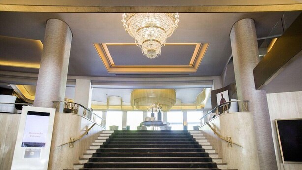 A grand staircase with a chandelier, marble columns, and a sign welcoming guests. - Tres Reyes Pamplona (Pamplona)