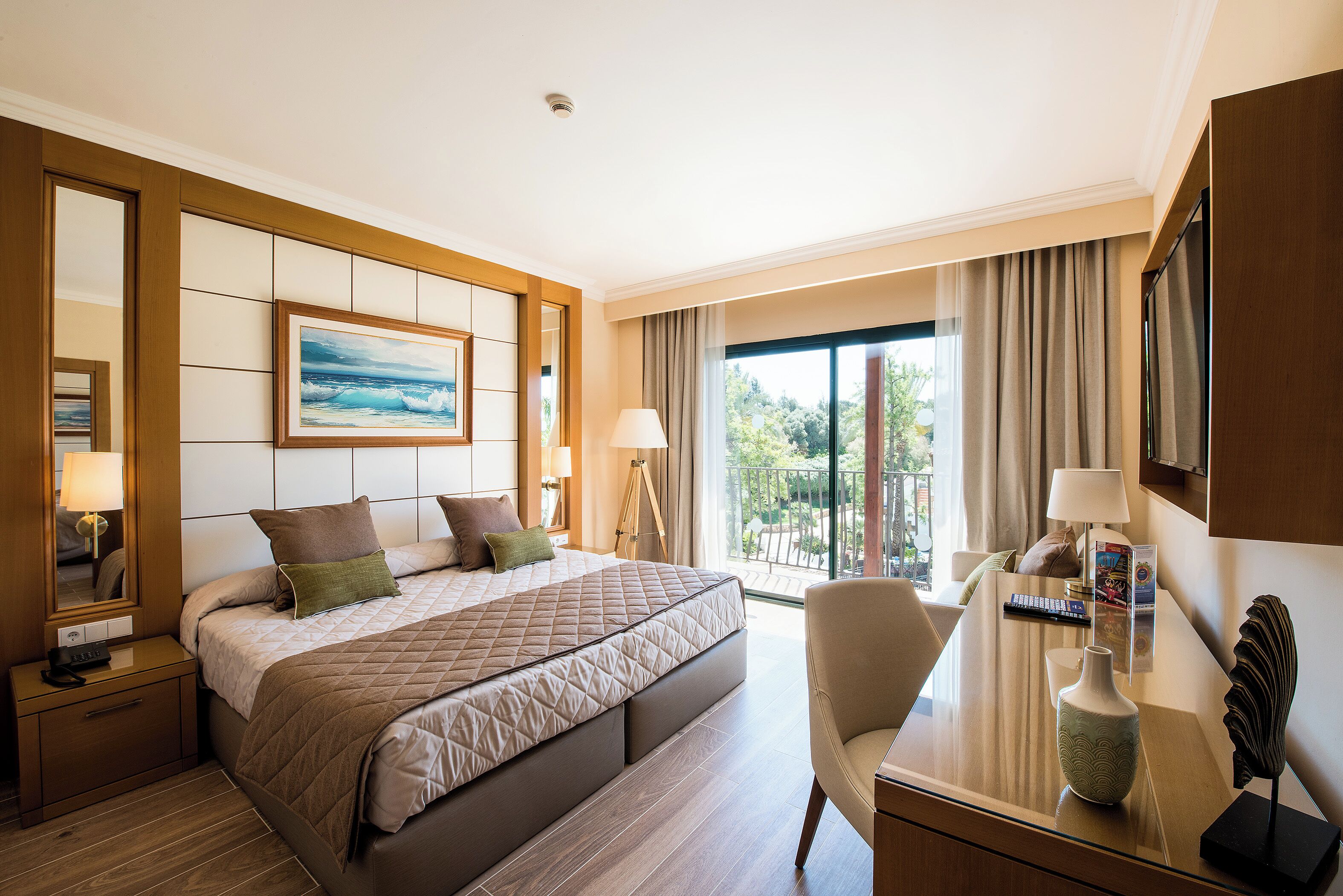 Habitación de hotel con una cama grande, un escritorio con un florero, una silla y un balcón con cortinas.