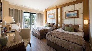 Ein Hotelzimmer mit zwei Betten, einem Schreibtisch mit Lampe, einem Sessel und Blick ins Freie.