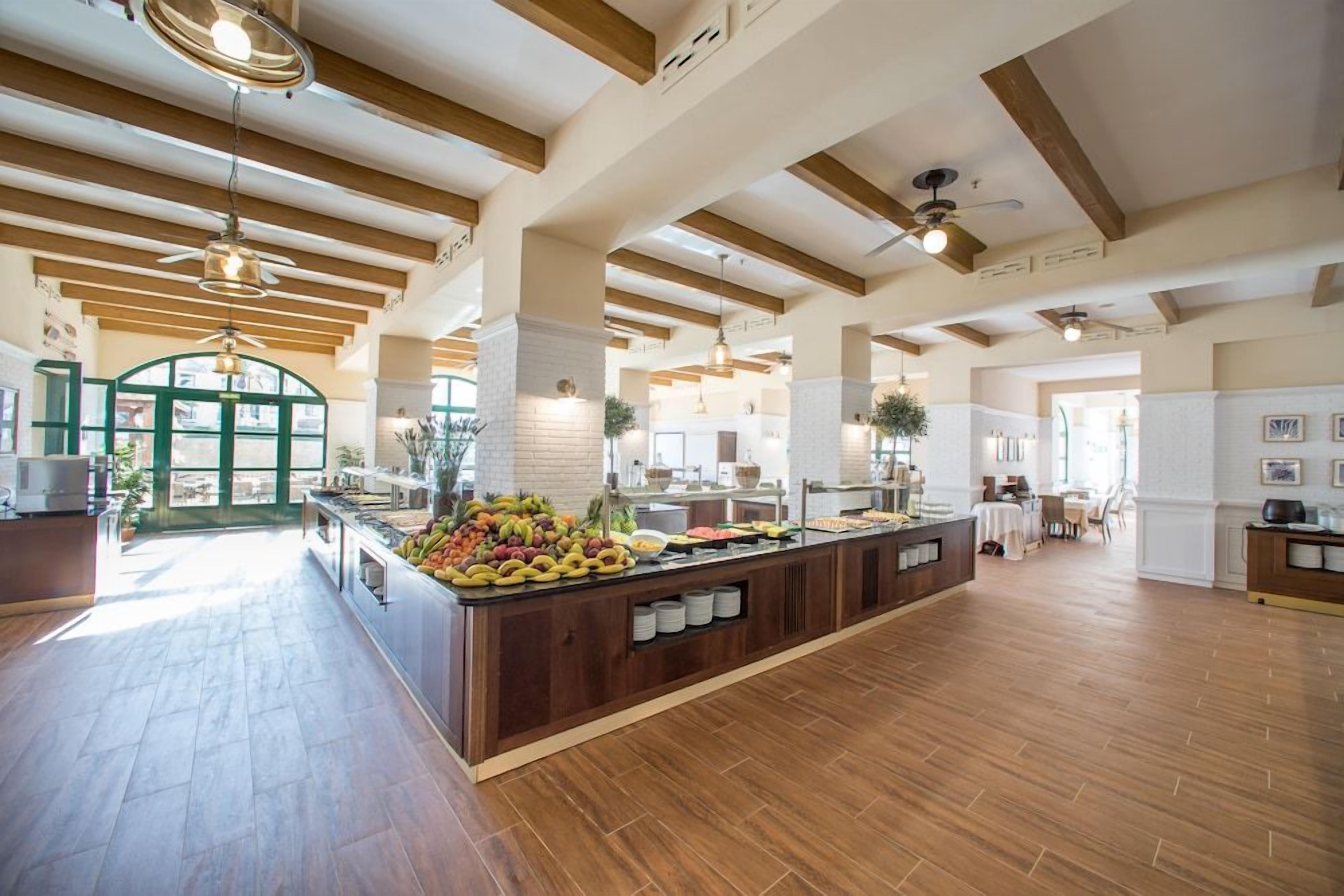Una cocina amplia con vigas de madera, una isla central con fruta y vistas al exterior.