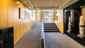 Un couloir d’hôtel moderne, avec un sol recouvert de moquette, des murs en bois et un escalier menant à un étage supérieur.