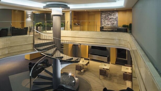 Un hall d’hôtel à plusieurs niveaux, doté d’un escalier en colimaçon central, de coins salon et d’une cheminée.