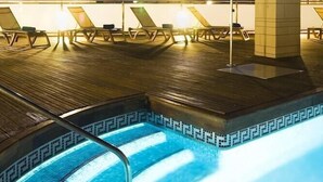 Un espace piscine aménagé sur le toit, avec des chaises longues et une vue sur le paysage urbain au crépuscule.