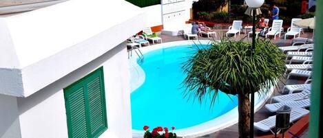 A pool area with white lounge chairs and a palm tree.
