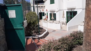 A white building with green shutters, a sign reading 'NIZA,' and outdoor seating with umbrellas. - Niza Apartments (Mogan)