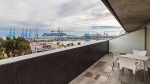 A balcony with a view of a port and cranes, featuring a table and chairs. - Suittes Hotel (Algeciras)