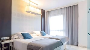 A modern hotel room with two beds, a bedside table, a lamp, and a large window with curtains. - Suittes Hotel (Algeciras)