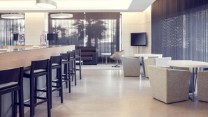 A modern hotel lobby with a long bar, seating area, and a TV screen. - Suittes Hotel (Algeciras)