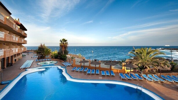 Ein Poolbereich mit Liegestühlen und Sonnenschirmen mit Blick auf das Meer.
