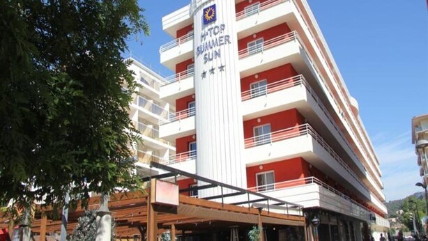 A multi-story hotel with balconies and a central column featuring the hotel's name. - H Top Secret-roulette 4 Santa Susanna (Santa Susanna)