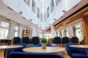 A modern interior with round tables and blue chairs, a central potted plant, and large windows allowing natural light. - Holiday Inn Express Logrono Rioja By IHG (Logroño)