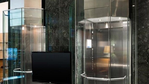 Two glass elevator cabins with metallic finishes, set against a marble wall, in a modern lobby. - Holiday Inn Express Logrono Rioja By IHG (Logroño)