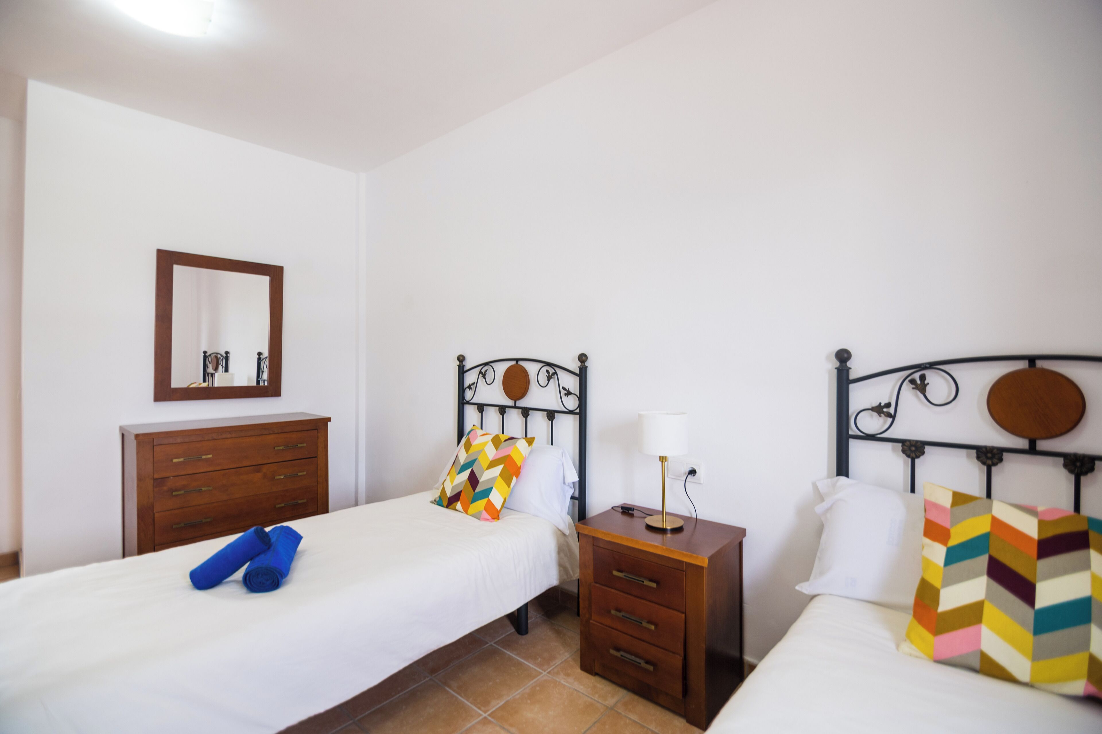 Une chambre d’hôtel avec deux lits, une commode en bois, une table de chevet avec une lampe et un miroir au mur.
