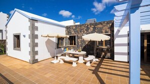 A patio with a table and benches, a stone wall, and a white building.
