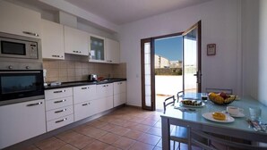 A modern kitchen with white cabinets, a microwave, and a stove. There's a dining area with a table and chairs, and a glass door leading outside.