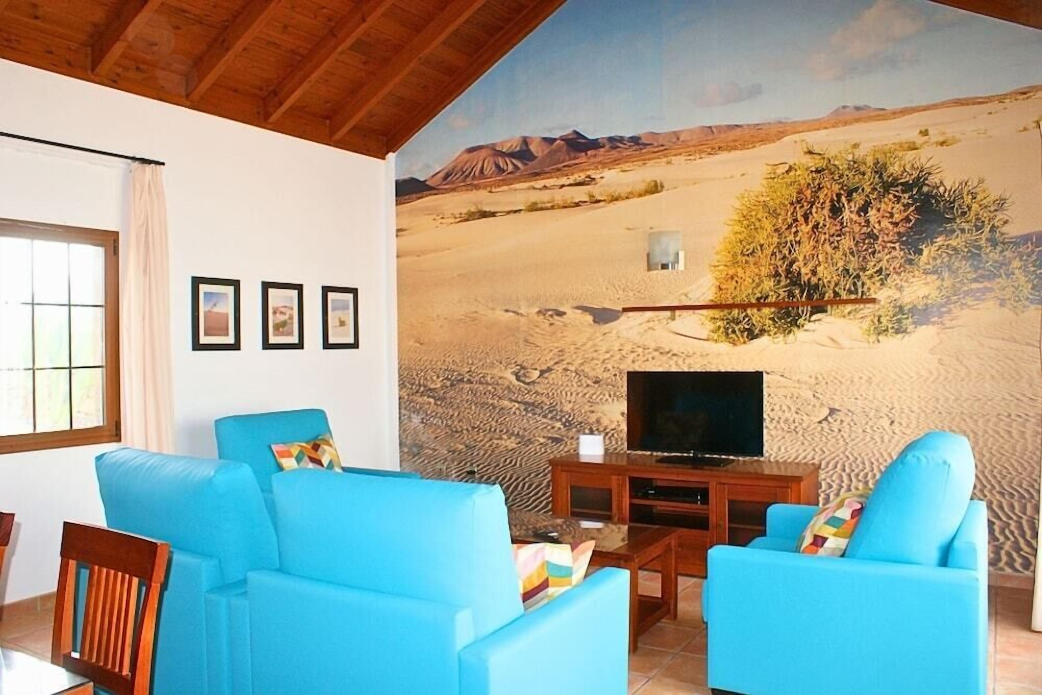 A living room with blue sofas, a TV, and a desert mural on the wall.