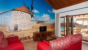 A room with a stone windmill mural, red sofas, a TV, and a pool view.