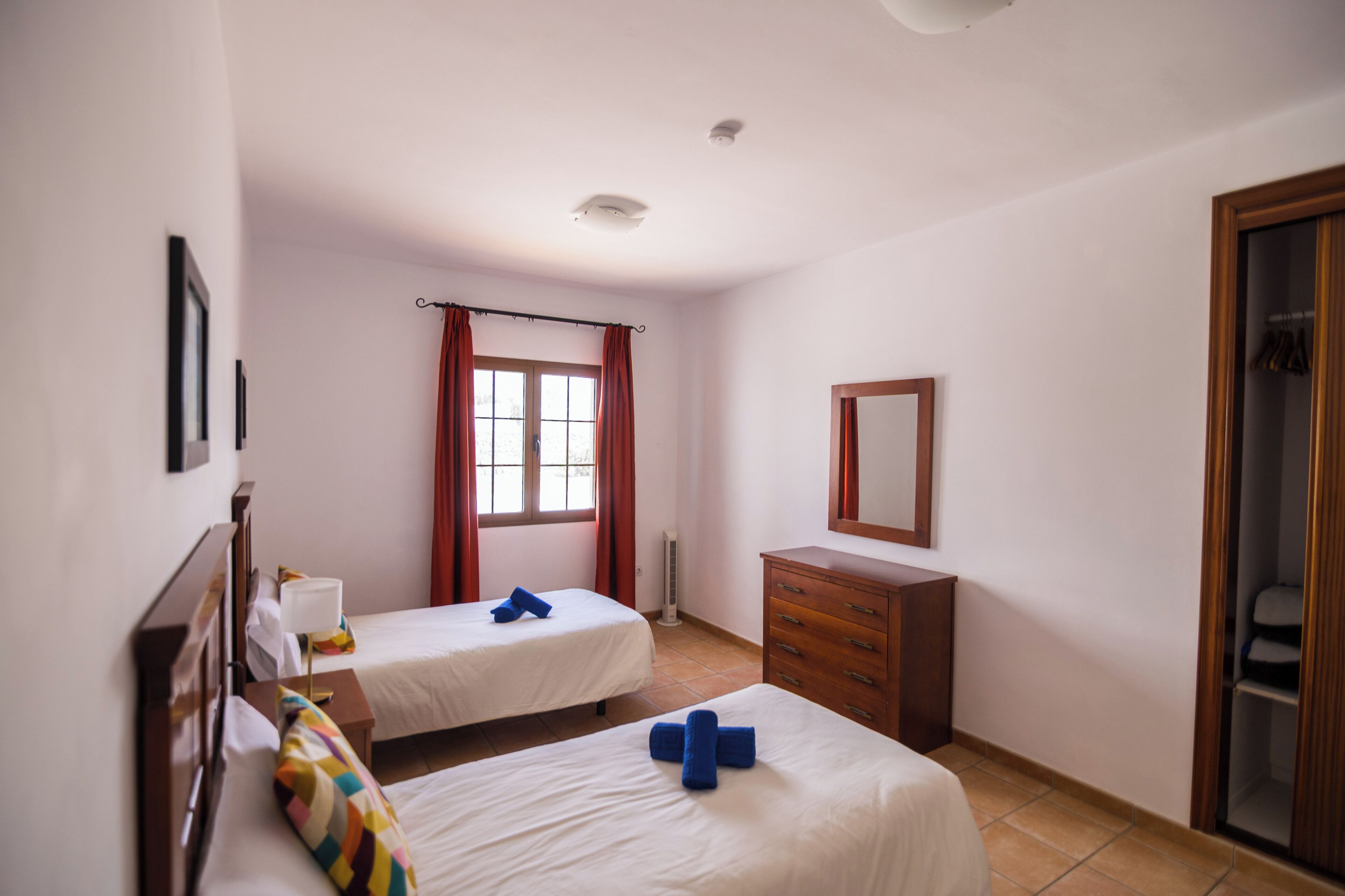 A hotel room with two beds, a wooden dresser, a mirror, and a window with curtains.