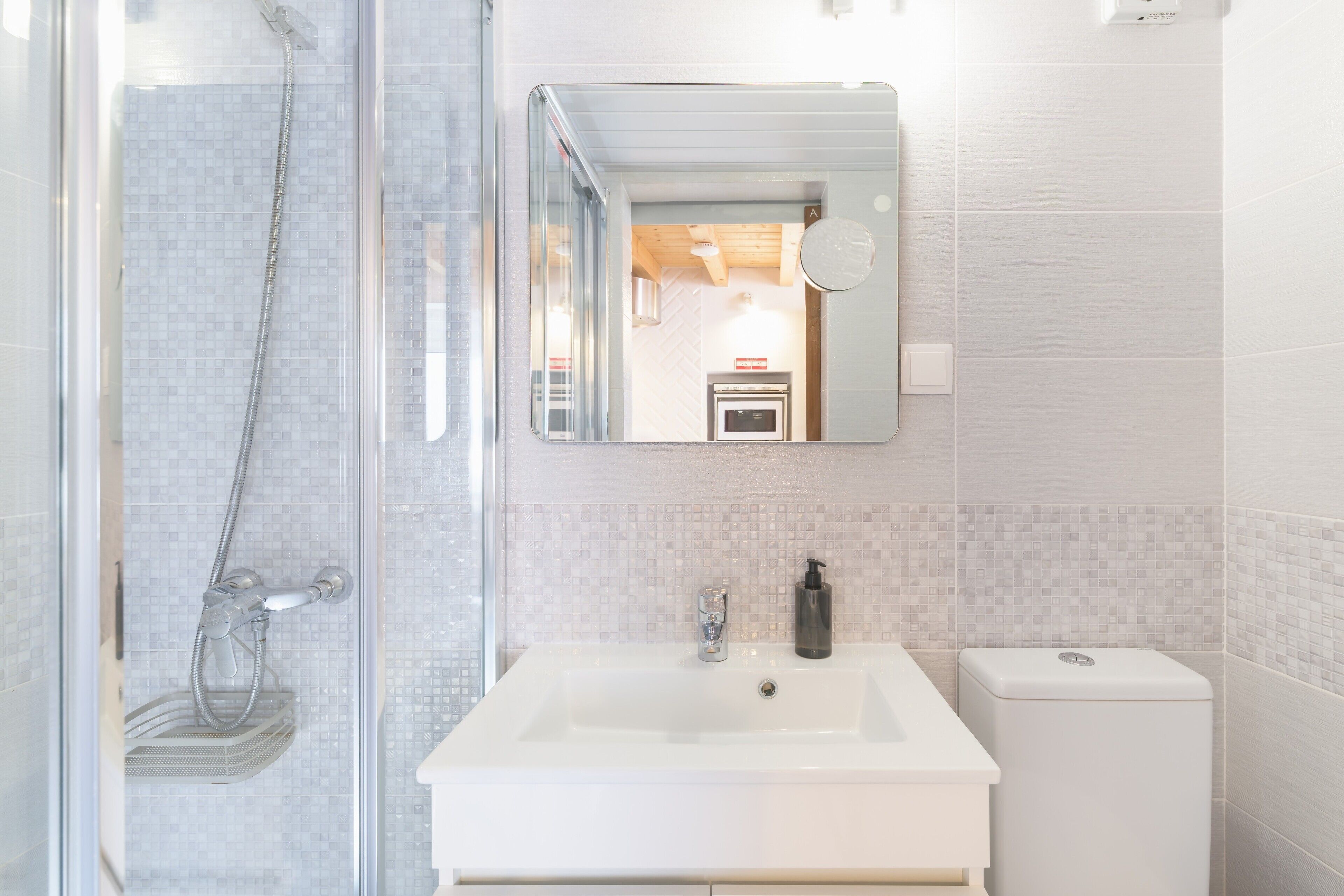 A bathroom with a glass shower enclosure, a white sink, a mirror, and a toilet.