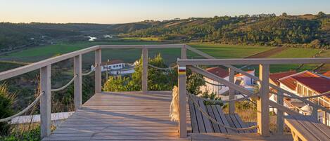 A wooden deck with a railing overlooking a valley with houses and a river.