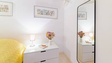 A bedroom with a bed, bedside table, mirror, and artwork on the wall.