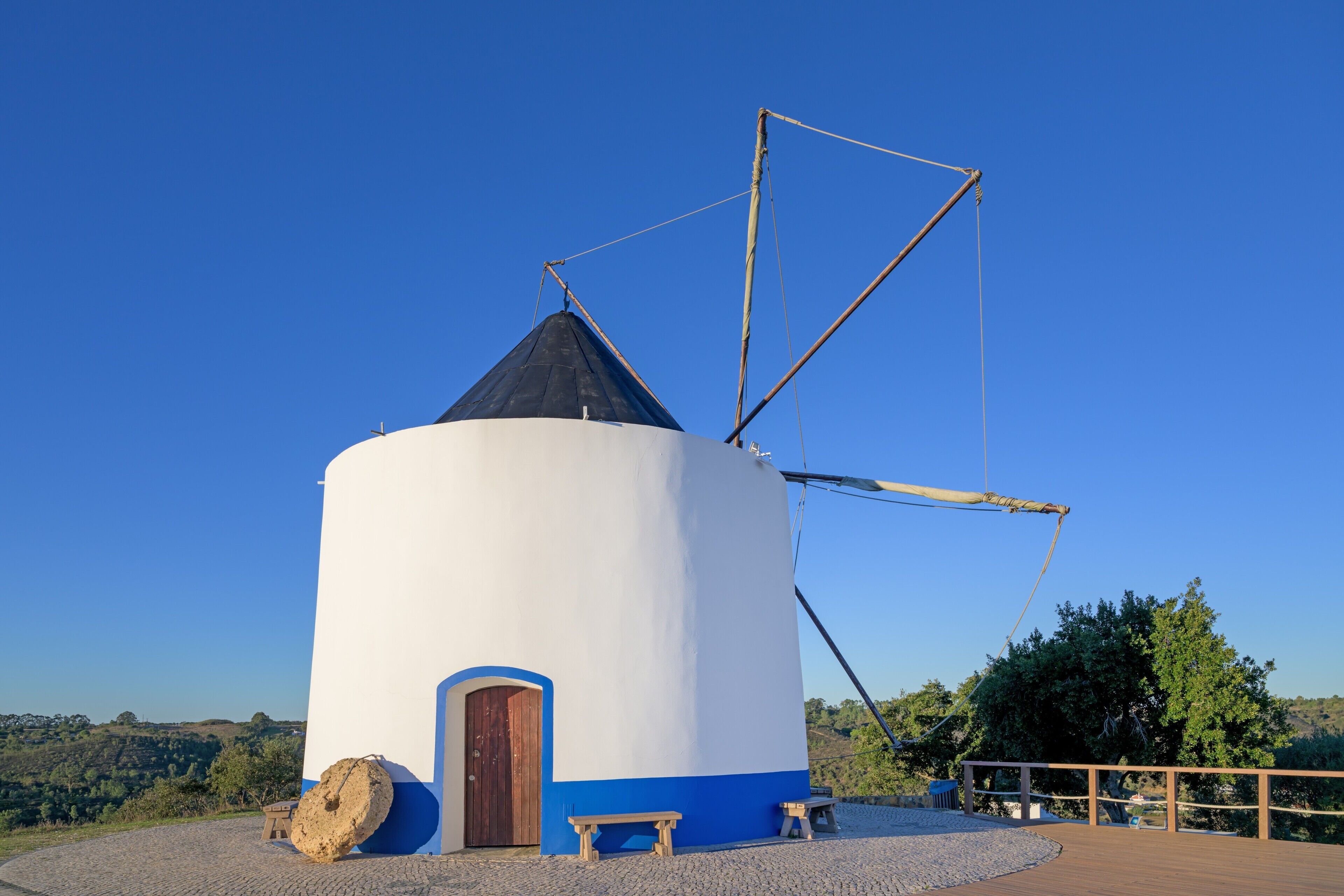 A windmill with a white and blue structure, a wooden door, and a bench.