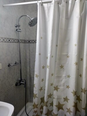 Un baño con ducha, una ducha de mano, toallero de pared y suelo de baldosas.