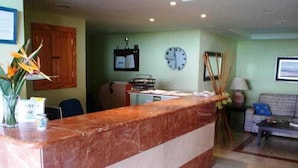 A reception desk with a marble top, a clock on the wall, and a sofa in the background. - Montemar Apartments (San Bartolomé de Tirajana)
