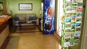 A reception area with a sofa, a coffee table, a wall-mounted picture, and a display of postcards. - Montemar Apartments (San Bartolomé de Tirajana)