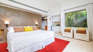 Ein Hotelzimmer mit einem großen Bett, einem roten Teppich, zwei weißen Sofas und einem großen Fenster mit Blick auf Grünflächen.