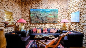 Ein Zimmer mit Steinwänden, einem Sofa, zwei Sesseln, einem Couchtisch und einem Bild an der Wand.