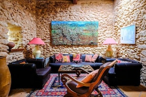 A stone-walled room with a sofa, two chairs, a coffee table, and a painting on the wall. - Can Lluc Boutique Country Hotel & Villas (Sant Antoni de Portmany)