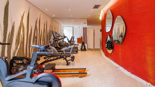 Ein modernes Fitnessstudio mit Ergometer, Laufbändern und einer roten Wand mit runden Spiegeln.
