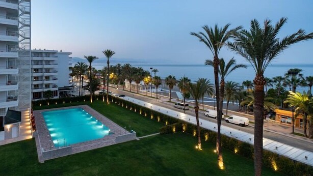 A hotel with a swimming pool, palm trees, and a view of the sea. - Hotel Apartamentos Bajondillo (Torremolinos)