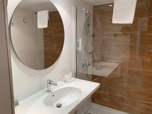 Un bagno moderno con uno specchio rotondo, un lavandino bianco, una doccia con pareti in vetro e piastrelle di legno.