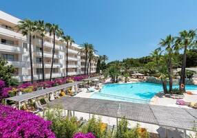 Un hotel con piscina rodeado de palmeras y flores coloridas.