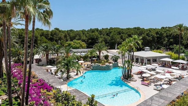 A large swimming pool surrounded by palm trees and lounge chairs, with a view of a forested area in the background. - Intelier Rosella Hotel (Sant Llorenc des Cardassar)
