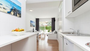 A modern kitchen with white countertops, a dining area with a white table and chairs, and a view of a garden through a glass door.