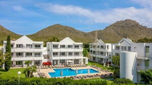 A resort with multiple white buildings, a central pool, and mountains in the background.