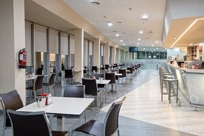 Een ruime eethoek met meerdere tafels en stoelen, een brandblusser aan de muur en een balie met een menukaart.