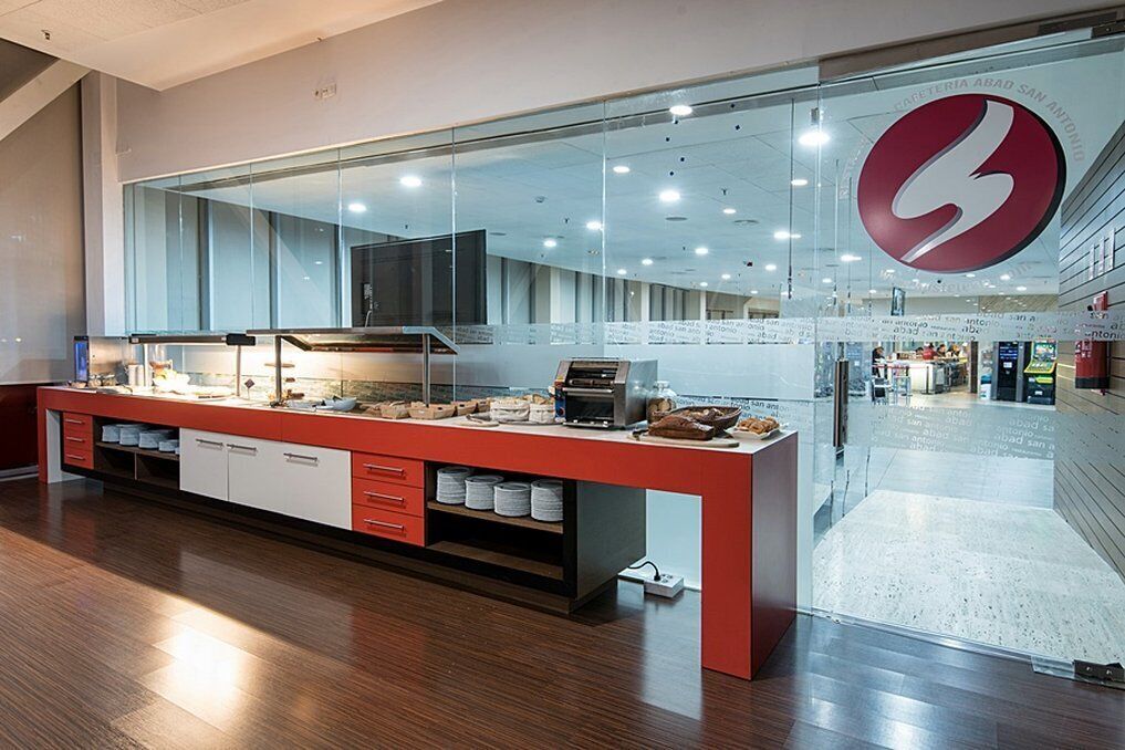 A modern kitchen with a red countertop, stainless steel appliances, and a glass wall with a logo.