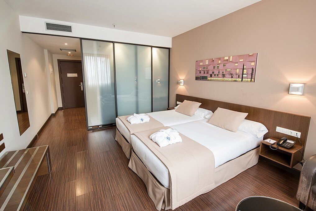 Habitación de hotel con una cama grande, una mesita de noche con teléfono, una lámpara de pared y un armario con puertas correderas.